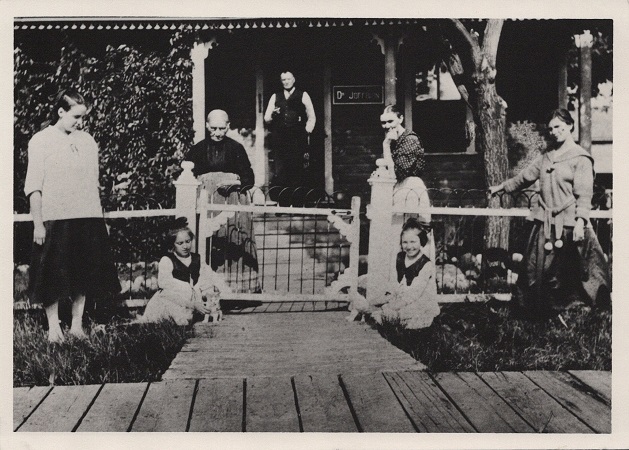Devant la résidence de Félix et Emma Grégoire à Saint-Jean-Baptiste. De de g. à dr. : leur fille Catherine; les jumelles Olivine et Oliva, filles d’Agathe et Honoré Mulaire alors décédés; et Mme Georges Haring, l’associé de Félix Grégoire. Derrière : Catherine Mulaire, le Dr Joffrion qui tenait bureau dans la résidence de Félix et Emma; et Emma Grégoire. Vers 1915. Archives provinciales du Manitoba.